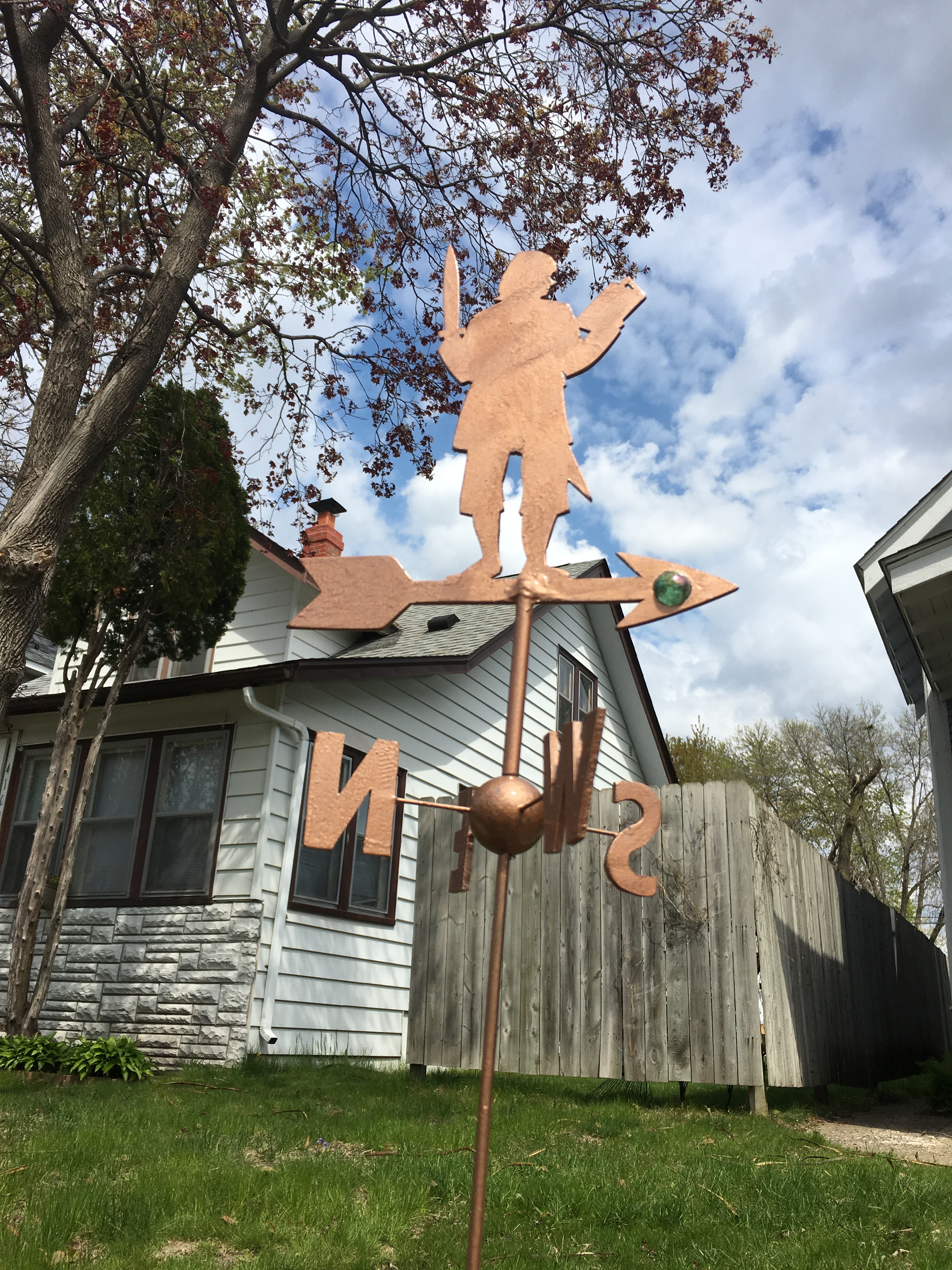 A weathervane shaped like a hobbit holding a sword in one hand and a book in the other